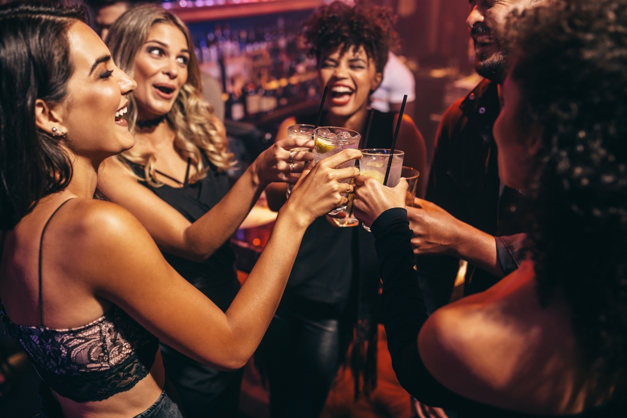 A group of friends in a bar clinking their drinks together for a toast. 