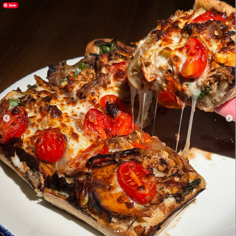 A close-up image of a slice of pizza with colorful toppings dripping with cheese.